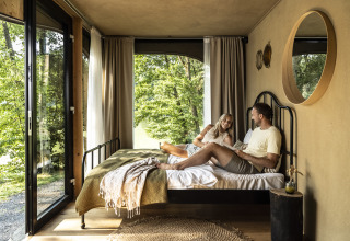 Un couple se détend dans un hébergement glamping moderne et lumineux avec vue sur la forêt chez Falkensteiner Premium Camping Blaguš en Slovénie.