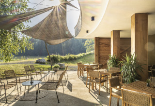 Udendørs spiseplads med moderne møbler, solsejl og udsigt til natur ved Falkensteiner Premium Camping Blaguš.