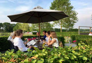 Comida al aire libre bajo sombrilla en De Betuwse Hofjes - Ranger Lodges Gelderland, rodeado de vegetación.