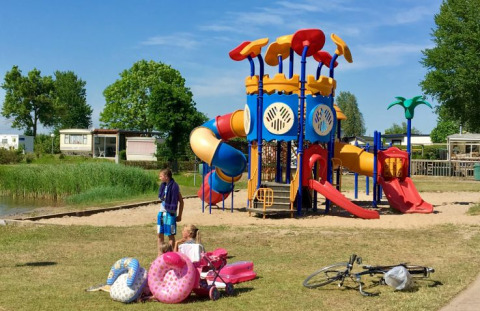 Parco giochi colorato con bambini, bici e passeggino davanti a De Betuwse Hofjes - Ranger Lodges Gelderland