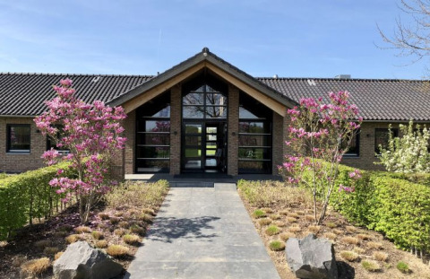 Indgang til De Betuwse Hofjes - Ranger Lodges Gelderland med smukke blomstrende træer og moderne bygning.