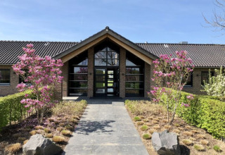 Ingang van De Betuwse Hofjes - Ranger Lodges Gelderland met bloeiende bomen en een modern lodgegebouw.