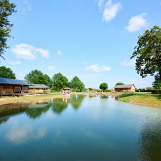 Glampingboliger ved en sø med træhytter og teltlignende lodges på De Betuwse Hofjes - Ranger Lodges Gelderland.