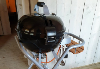 Zwarte bolbarbecue met deksel en gereedschap op houten plankjes bij De Betuwse Hofjes - Ranger Lodges Gelderland.