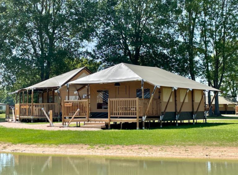 Twee glamping Ranger Lodges aan het water bij De Betuwse Hofjes in Gelderland, omgeven door groene bomen.