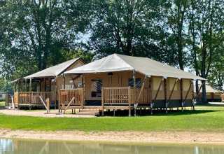 Dos alojamientos glamping Ranger Lodges junto al agua en De Betuwse Hofjes, Gelderland, rodeados de árboles verdes.