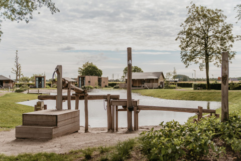 Glamping De Betuwse Hofjes - Ranger Lodges Gelderland con area giochi in legno e vista sul laghetto naturale.