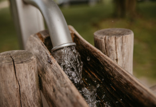 Vand løber fra et rør ned i en trævask på De Betuwse Hofjes - Ranger Lodges Gelderland glampingplads.