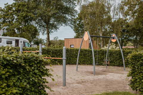 Playground with swings and climbing bars near a modern glamping cabin at De Betuwse Hofjes - Ranger Lodges Gelderland.