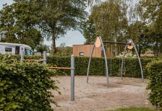 Parque infantil con columpios y barras junto a una cabaña moderna en De Betuwse Hofjes - Ranger Lodges Gelderland.