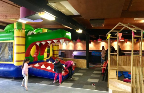 Indoor playground at De Betuwse Hofjes with inflatable crocodile bounce house, kids playing, and festive bunting.