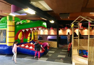 Aire de jeux intérieure à De Betuwse Hofjes avec structure gonflable crocodile, enfants et fanions colorés.