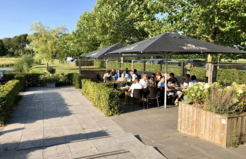 Area pranzo all'aperto presso De Betuwse Hofjes - Ranger Lodges Gelderland con ospiti seduti sotto ombrelloni neri.