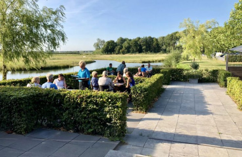 Zona de comedor exterior en De Betuwse Hofjes - Ranger Lodges Gelderland, junto a un río y campo verde.