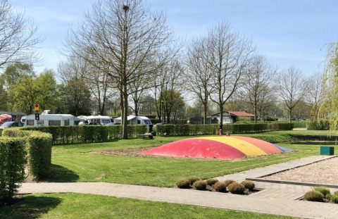 Campingplatz mit Hüpfkissen und Wohnwagen bei De Betuwse Hofjes - Ranger Lodges Gelderland im Sonnenschein.