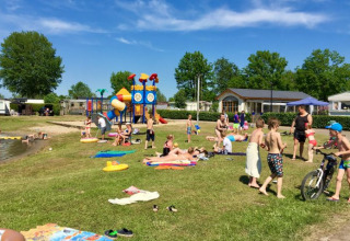 Famiglie si divertono all'aperto a De Betuwse Hofjes - Ranger Lodges Gelderland con parco giochi e lago.