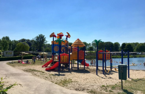 Área de juegos y playa en De Betuwse Hofjes - Ranger Lodges Gelderland glamping bajo un cielo soleado.