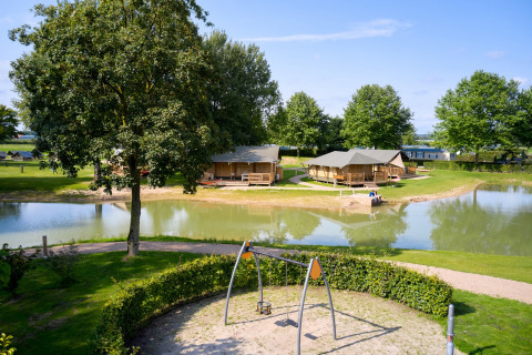 Glamping a De Betuwse Hofjes - Ranger Lodges Gelderland, tende sul lago e parco giochi visibile.