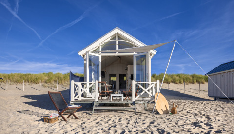 Luxury beach house accommodation in The Hague with sunshade, outdoor furniture and sandy surroundings.
