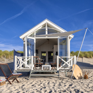 Luxe strandhuisje in Den Haag met zonnescherm, terrasstoelen en prachtig zicht op de zandduinen.
