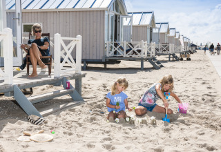 Familie genießt Luxus-Strandhäuser am Strand, während Kinder im Sand spielen und Erwachsene entspannen.