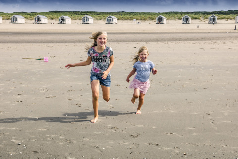 Due bambini felici corrono sulla spiaggia davanti alle lussuose case di HaagseStrandhuisjes a L'Aia.