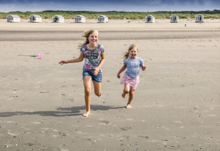Twee vrolijke kinderen rennen op het strand voor de luxe strandhuisjes van HaagseStrandhuisjes in Den Haag.