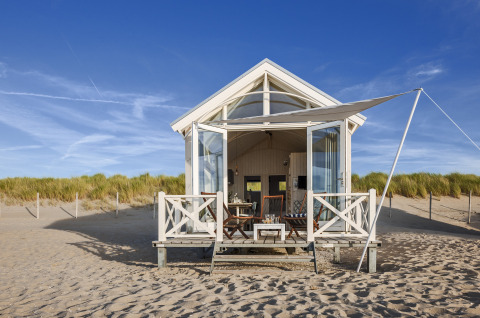 A luxury beach cabin from HaagseStrandhuisjes on the sandy shores of The Hague, set against a blue sky.