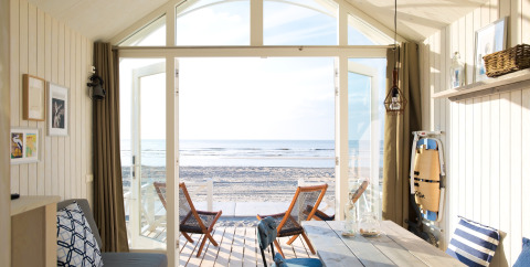 Casa sulla spiaggia moderna con porte aperte sulla sabbia, arredi accoglienti e splendida vista mare.
