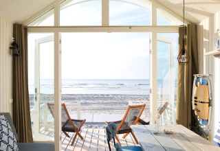 Cabane de plage moderne avec portes vitrées ouvertes donnant sur la mer, cadre lumineux et confortable.