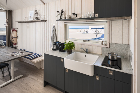 Moderne glamping strandhytte i Den Haag med køkken og udsigt til stranden gennem vinduet.