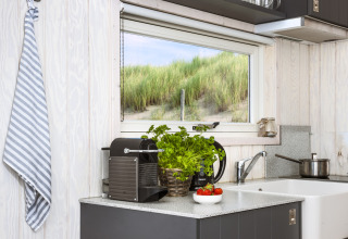 Moderne Campingküche mit Kaffeemaschine, Kräutern und Fensterblick auf Dünen bei den Haag.