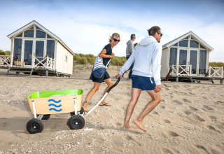 Famiglia che trascina un carrello sulla sabbia davanti a lussuose case sulla spiaggia di HaagseStrandhuisjes a L'Aia.