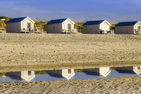 Quatre cabanes de plage de luxe au toit bleu à La Haye, idéales pour un séjour glamping en bord de mer.