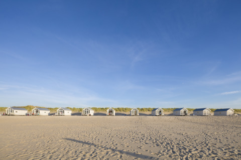 Rij luxe strandhuisjes op het zand in Den Haag, ideaal voor glamping en bijzonder overnachten aan zee.
