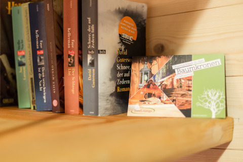 Libri su uno scaffale con una carta TreeLounge che promuove il glamping in case sugli alberi a Cuxhaven.