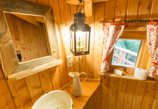 Binnenkant van boomhut met wasbak, spiegel, lantaarn en raam, TreeLounge Boomhut Nedersaksen glamping.