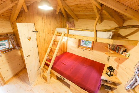 Cozy interior of a treehouse glamping accommodation with bunk beds, wood paneling and scenic windows.