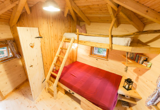 Cozy interior of a treehouse glamping accommodation with bunk beds, wood paneling and scenic windows.