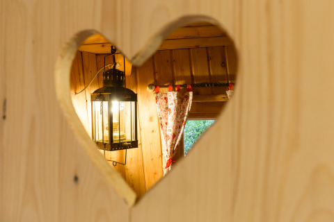 Vista attraverso un ritaglio a forma di cuore su lanterna e tende in TreeLounge - Boomhut Nedersaksen.