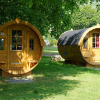Two luxury barrel-shaped glamping cabins at Mosel Islands campsite, set in green parkland, summer day.