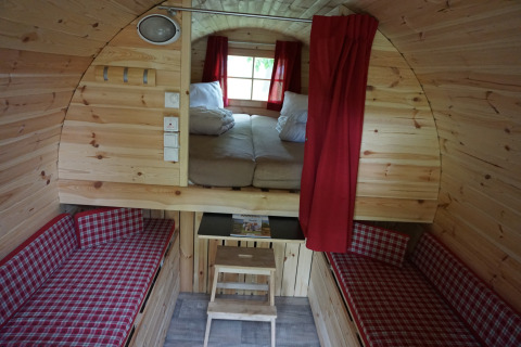 Intérieur d’un tonneau en bois glamping avec lit double, deux canapés et rideaux rouges aux îles Mosel.