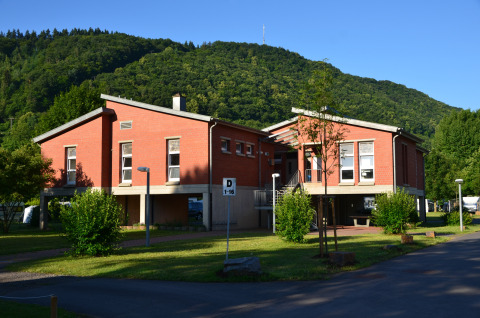 Glamping ved Moselfloden med moderne røde bygninger omgivet af grønne bakker og træer i solskin.