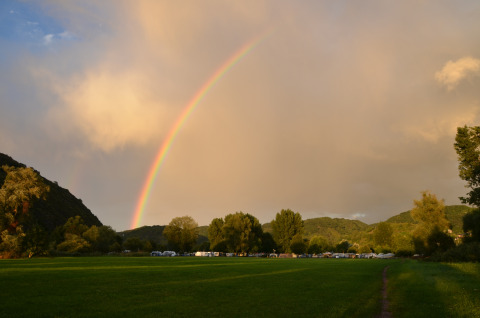 Glamping Mosel Islands con dormitorios de lujo junto al río y un arcoíris sobre campos verdes al atardecer.