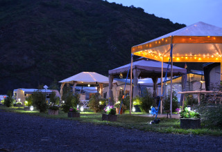 Alloggio glamping Mosel Islands vicino al Mosella con tende illuminate e piante al tramonto.