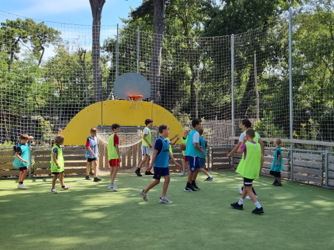 Kinderen spelen basketbal op een omheind veld bij Camping Les Cyprès - Glampingtenten Vendée.