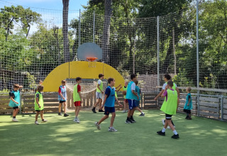 Børn spiller basketball på en udendørs bane omgivet af net ved Camping Les Cyprès - Glampingtenten Vendée.