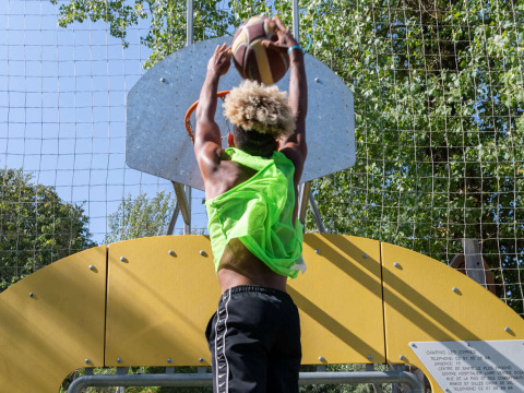 Persona che gioca a basket e tenta una schiacciata su un campo all'aperto al Camping Les Cyprès - Glampingtenten Vendée.