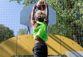 Persona che gioca a basket e tenta una schiacciata su un campo all'aperto al Camping Les Cyprès - Glampingtenten Vendée.
