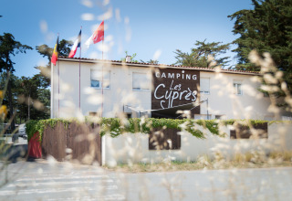 Ingang van Camping Les Cyprès - Glampingtenten Vendée met vlaggen, gebouw en bomen in de omgeving.